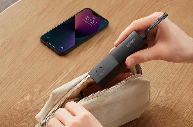 A charger is entering a beige small bag with an iPhone in the background. 