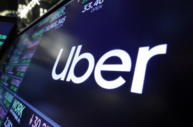 The logo for Uber appears above a trading post on the floor of the New York Stock Exchange, Aug. 16, 2019. The ride-hailing and delivery company said Wednesday, Oct. 4, 2023, that its drivers will collect up to five prepaid and sealed packages and drop them off at a local post office or at UPS or FedEx stores. Uber will charge a flat fee of $5 for the service or $3 for its Uber One members. (AP Photo/Richard Drew, File)