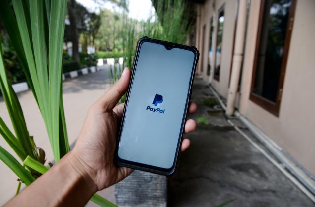A man seen hold a smartphone with the logo PayPal in Bogor, West Java, Indonesia on July 30, 2022. The Indonesian Ministry of Communication and Information has blocked several applications related to the registration of Electronic System Operators (PSE) as an effort by the Indonesian government to protect public consumers, including PayPal Inc platform. (Photo by Adriana Adie/NurPhoto via Getty Images)